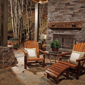 A large patio with stone and wood details includes wooden chairs and a fireplace in the seating area.