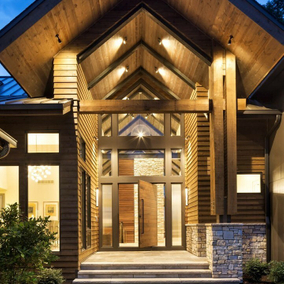Front entryway of a home with a wood exterior and exposed beams. The front door is a large pivot-style wood door that’s open and leads into the home.